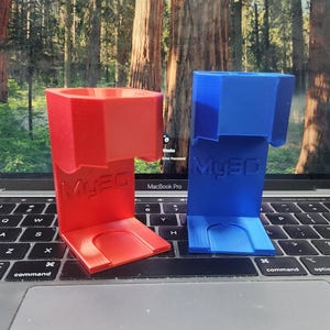 May include: Two 3D printed phone stands, one red and one blue, with the word "MY3D" printed on the front. The stands are sitting on a laptop keyboard.