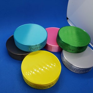 May include: Six round, colorful, 3D printed containers with a textured surface. The containers are in various colors, including teal, pink, green, yellow, black, and silver.