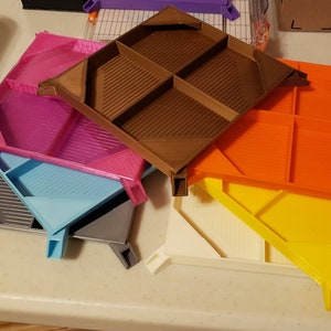 Può includere: Cinque vassoi stampati in 3D in diversi colori, tra cui rosa, blu, arancione, giallo e bianco. I vassoi hanno un motivo a griglia e sono impilati uno sopra l'altro.