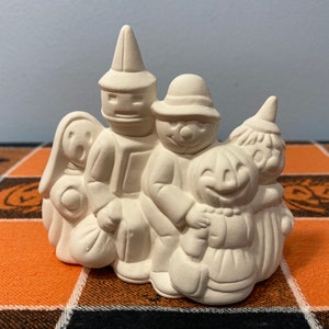 Puede incluir: Una figura de cer&aacute;mica de Halloween que representa un grupo de figuras disfrazadas. Las figuras incluyen un fantasma, un mago, un ni&ntilde;o con sombrero, una calabaza y una bruja. La figura no est&aacute; pintada y est&aacute; lista para personalizar.
