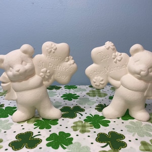May include: Two white ceramic bear figurines holding shamrock-shaped signs. One sign reads "Happy St. Patrick's Day!" and the other reads "Top o' the Mornin'"