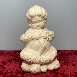 May include: White ceramic figurine of a woman knitting with yarn balls at her feet. The woman is wearing a hat and glasses.