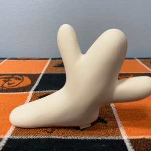 Puede incluir: Una escultura de cer&aacute;mica de color crema en forma estilizada y abstracta. La escultura tiene una superficie lisa y una forma &uacute;nica con m&uacute;ltiples proyecciones redondeadas. Se encuentra sobre una superficie a cuadros naranja, negro y blanco.