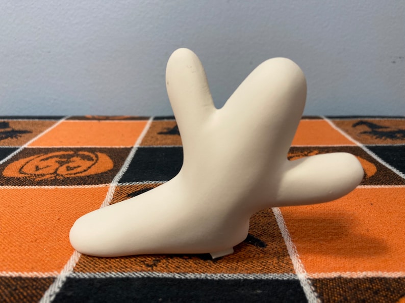 Puede incluir: Una escultura de cer&aacute;mica de color crema en forma estilizada y abstracta. La escultura tiene una superficie lisa y una forma &uacute;nica con m&uacute;ltiples proyecciones redondeadas. Se encuentra sobre una superficie a cuadros naranja, negro y blanco.