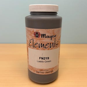 May include: A cylindrical plastic bottle containing Mayco Elements FN219 Lustre Green glaze. The label features the brand name, product code, and color name. The bottle has a white screw-top lid and a volume capacity of 16 fl oz (473ml).