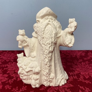 May include: White ceramic figurine of Santa Claus holding a bag of teddy bears. Santa is wearing a hat and a long coat with a fur trim.