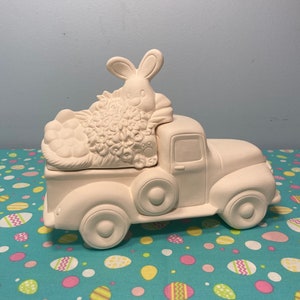 May include: White ceramic pick-up truck with a bunny and flowers in the back. The truck is ready to be painted.