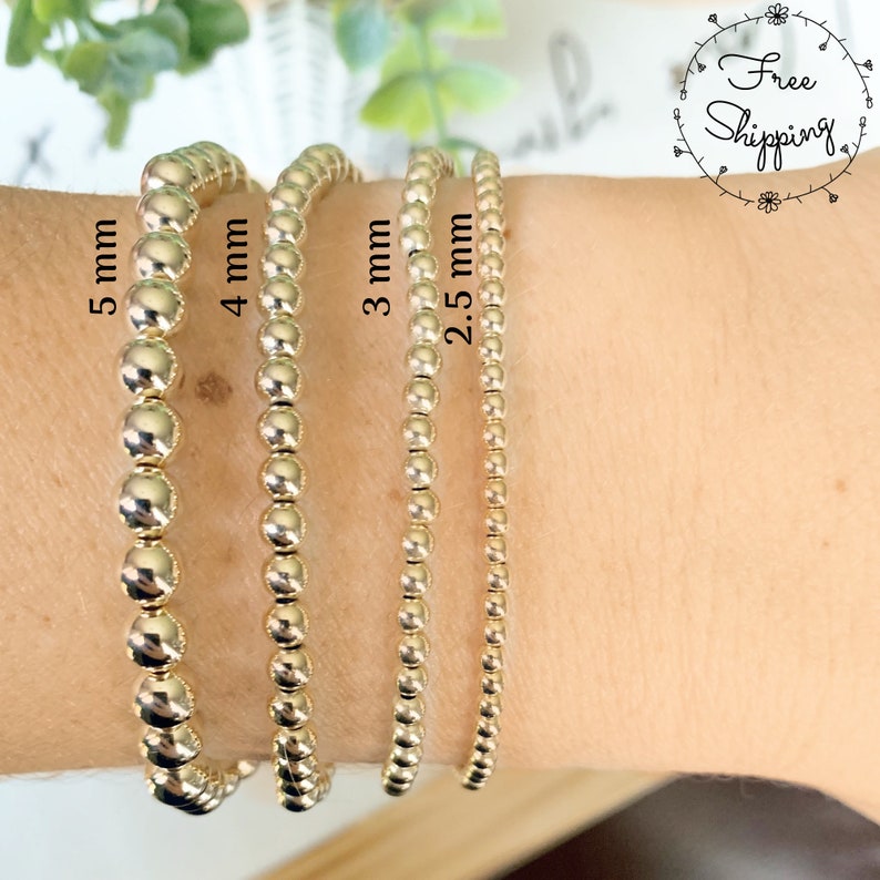 May include: Four gold beaded bracelets, each with different bead sizes: 5 mm, 4 mm, 3 mm, and 2.5 mm. The bracelets are displayed on a wrist, showcasing the varying sizes of the gold beads. The image includes the text "Free Shipping".