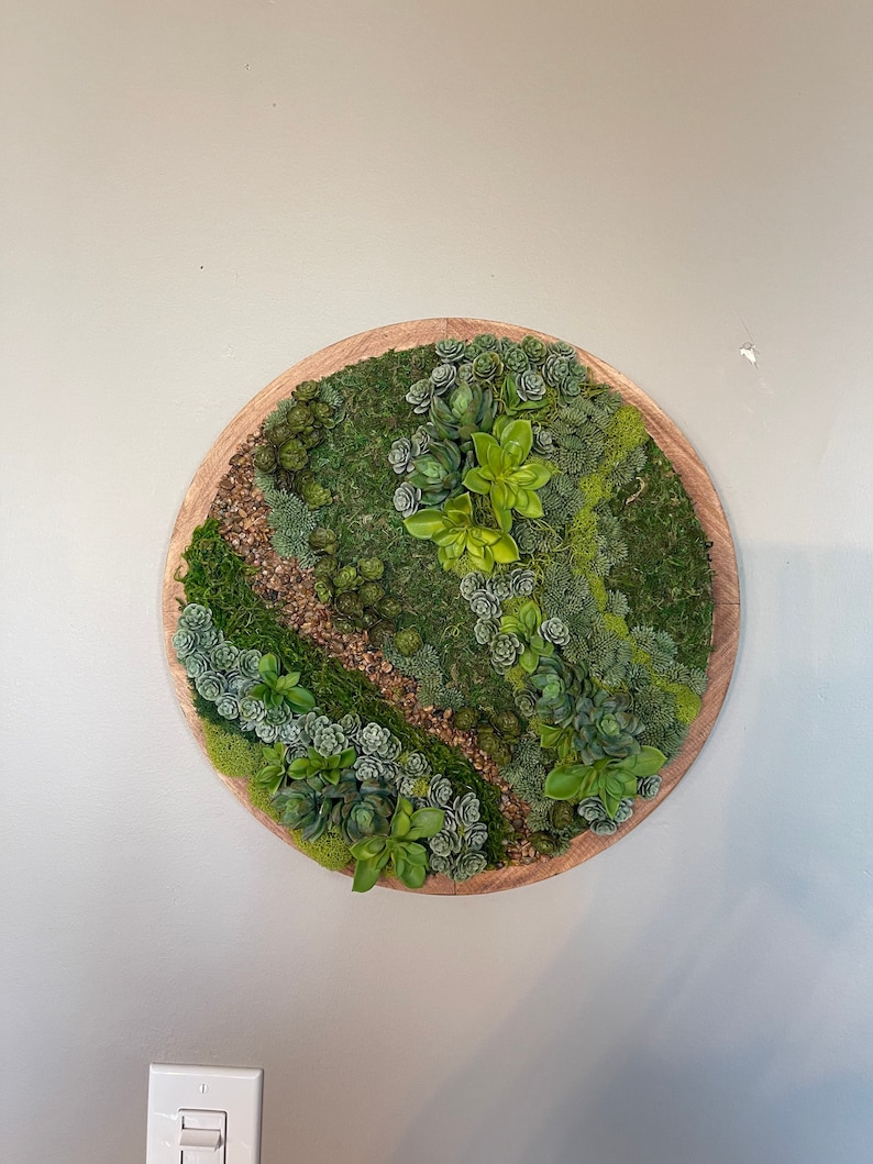 May include: A round wooden wall decor piece featuring a variety of green succulents and moss arranged in a circular pattern.