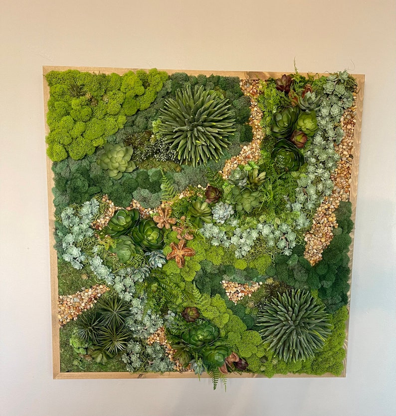 Puede incluir: Una pieza de arte de pared enmarcada de musgo verde y suculentas. La pieza presenta una variedad de suculentas y musgo verdes, dispuestos en un patr&oacute;n natural y org&aacute;nico. El marco es de madera y tiene un acabado natural.