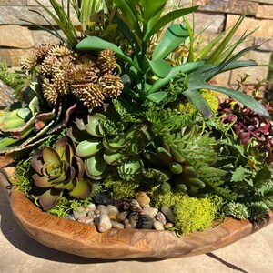 May include: A wooden bowl filled with a variety of green succulents and moss. The bowl is decorated with small, smooth stones.