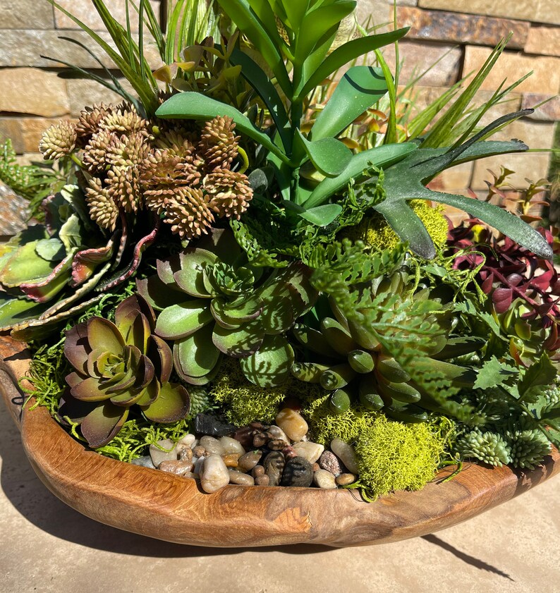 May include: A wooden bowl filled with a variety of green succulents and moss. The bowl is decorated with small, smooth stones.