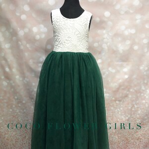 Puede incluir: Un corpi&ntilde;o blanco de encaje sin mangas con una falda de tul verde. El vestido est&aacute; en un maniqu&iacute; y el fondo es rosa brillante.
