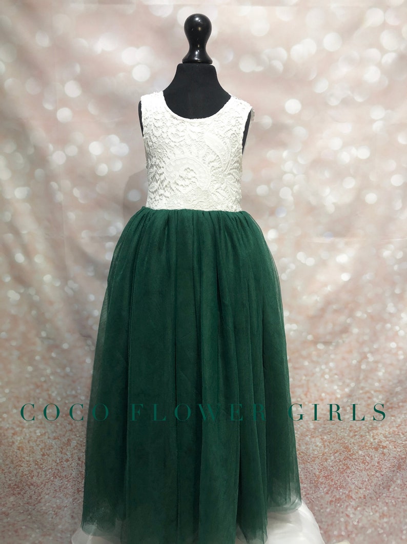 Puede incluir: Un corpi&ntilde;o blanco de encaje sin mangas con una falda de tul verde. El vestido est&aacute; en un maniqu&iacute; y el fondo es rosa brillante.