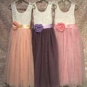 Puede incluir: Tres vestidos de ni&ntilde;a de las flores de tul con corpi&ntilde;o de encaje y cinta de sat&eacute;n. Los vestidos son en melocot&oacute;n, malva y rosa.