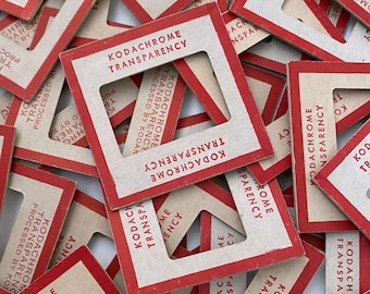 May include: A collection of vintage Kodachrome transparency mounts. Each mount is rectangular with a red border and a central square opening. The text "KODACHROME TRANSPARENCY" is printed in red on each mount, along with "PROCESSED BY KODAK".