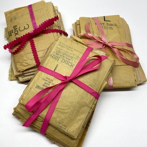 May include: Three bundles of vintage sewing patterns wrapped in brown paper and tied with pink ribbon. The bundles are labeled "Back", "Vest Pack", and "Shirt Back".