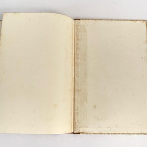 May include: An open book with aged, off-white pages. The pages show signs of wear and age, with a slightly yellowed tone and subtle spotting. The book's binding is visible, with a light brown color. The book is open, displaying the blank pages.
