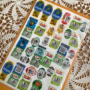 May include: A collection of assorted produce stickers on a rectangular sheet, featuring various brand logos including Chiquita, Dole, and Del Monte, alongside Minecraft-themed labels, barcodes, and numerical product codes for fruits and vegetables.