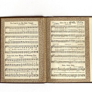 May include: An open book of sheet music with brown covers and decorative patterned endpapers. The left page features the title "The Lord Is in His Holy Temple" and "Praise God, from Whom All Blessings Flow." The right page is titled "Glory Be to the Father" and "Holy, Holy, Holy."