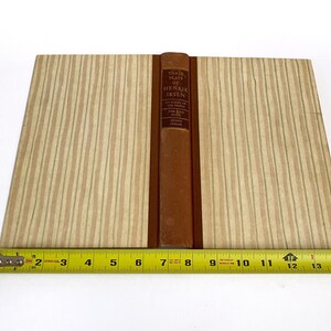 May include: A vintage book titled "Three Plays of Henrik Ibsen" with a brown leather spine and tan striped covers. A yellow measuring tape is placed below the book, showing measurements in inches.