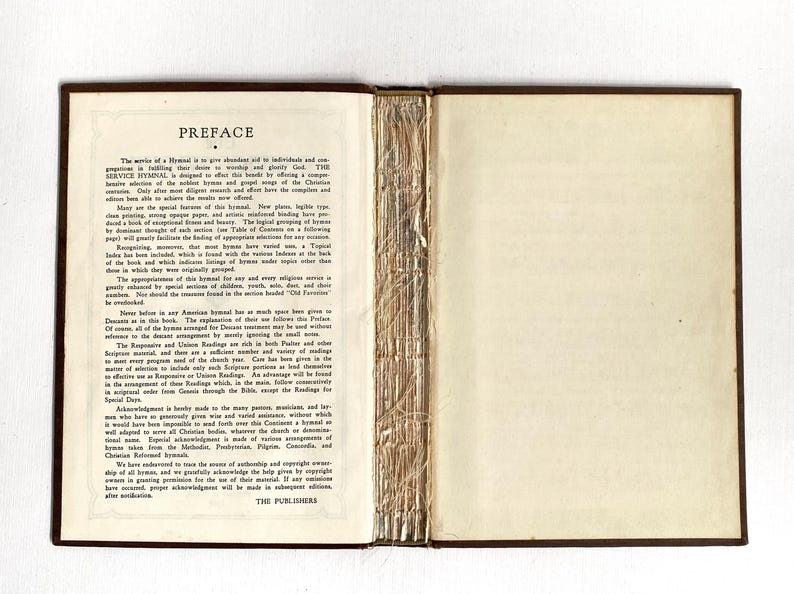 May include: Open vintage book with a brown cover and gold-colored binding. The left page displays the title "PREFACE" and text. The right page is blank. The book is open, revealing the pages and spine.