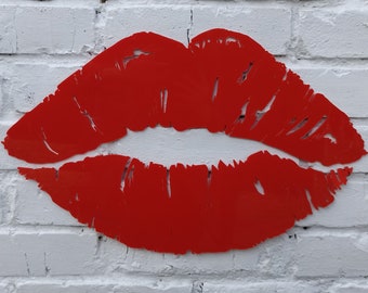 Può includere: Un grande ritaglio di metallo rosso a forma di labbra su un muro di mattoni bianchi.