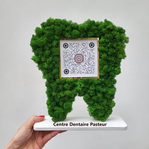 Peut inclure: Une sculpture en mousse verte en forme de dent, avec un code QR et le logo Instagram sur un carré encadré d'or. La sculpture est montée sur une base blanche avec le texte "Centre Dentaire Pasteur".