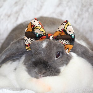 以下が含まれることがあります： 垂れ耳のグレーと白のウサギが、ハリーポッターをテーマにしたカラフルな蝶ネクタイをしています。