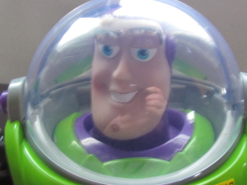 Puede incluir: Primer plano de una figura de acci&oacute;n de Buzz Lightyear. El juguete tiene un traje espacial verde y morado con un casco transparente. La cara de la figura es de color rosa claro con ojos azules y una ligera sonrisa. El tema general son los juguetes y objetos de colecci&oacute;n.