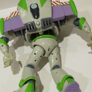 May include: A Buzz Lightyear action figure, featuring a white and green spacesuit with purple accents. The toy has articulated limbs and a jetpack with red and white stripes. The figure is posed on a white surface.