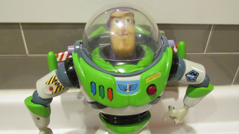 May include: A Buzz Lightyear action figure, featuring a green and white spacesuit with a clear helmet. The figure has the word "LIGHTYEAR" on the chest and a red button. The figure's arms are outstretched, and it has a determined expression.