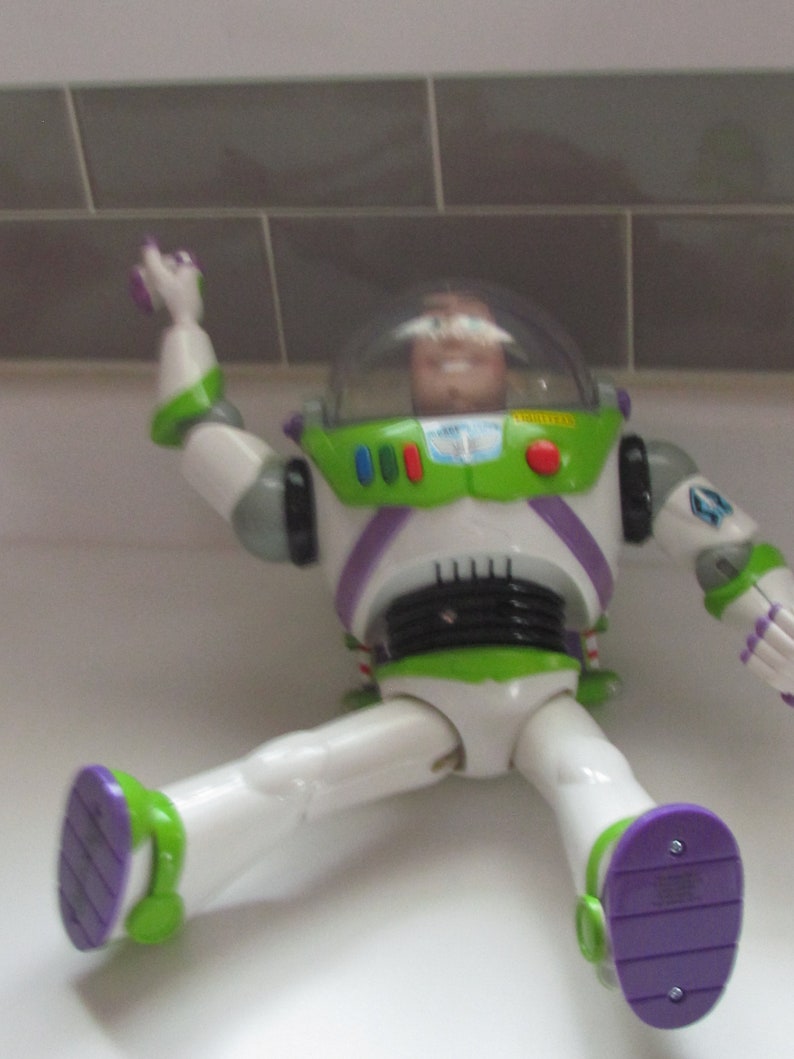 Puede incluir: Figura de acci&oacute;n de Buzz Lightyear en posici&oacute;n sentada. El juguete presenta un traje espacial blanco y verde con detalles morados. La figura tiene un casco transparente y es un art&iacute;culo de colecci&oacute;n de la franquicia Toy Story.