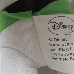 May include: White plush toy with green and black details. The toy has a tag that reads "Disney" and "&copy;Disney Manufactured under Just Play, LLC 401 Fairway Drive, Deerfield Beach, FL".