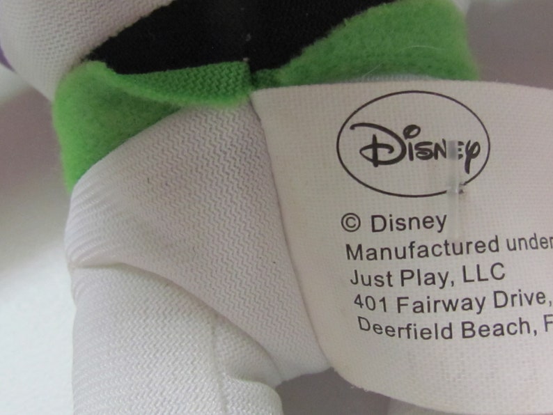 May include: White plush toy with green and black details. The toy has a tag that reads "Disney" and "&copy;Disney Manufactured under Just Play, LLC 401 Fairway Drive, Deerfield Beach, FL".
