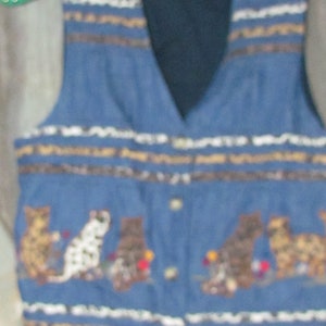 Puede incluir: Un chaleco vaquero azul con un patrón de rayas marrones, blancas y negras. El chaleco tiene cuello en V y está decorado con imágenes bordadas de gatos.