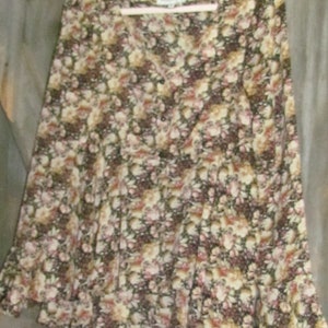 May include: A long-sleeved blouse with a floral pattern in shades of brown, cream, and pink. The blouse has a V-neck and a ruffled hem. The garment is hanging on a white hanger.