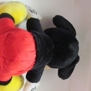 May include: A plush Mickey Mouse toy, featuring a red shorts, black body, yellow shoes, and white gloves. The toy is lying on its side, showcasing its iconic design and colors. A classic Disney character.