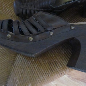 May include: Brown leather platform sandals with a woven design and metal accents. The sandals have a thick wooden platform sole and a high heel.