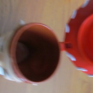 May include: A red and white ceramic piggy bank with a hinged lid. The lid is open and the inside of the bank is visible.