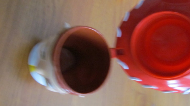 May include: A red and white ceramic piggy bank with a hinged lid. The lid is open and the inside of the bank is visible.
