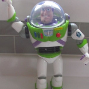 Puede incluir: Figura de acci&oacute;n de Buzz Lightyear de la franquicia Toy Story. La figura es principalmente blanca, verde y morada, con un casco de pl&aacute;stico transparente. Tiene brazos y piernas articulados, y la cara de Buzz Lightyear es visible dentro del casco.