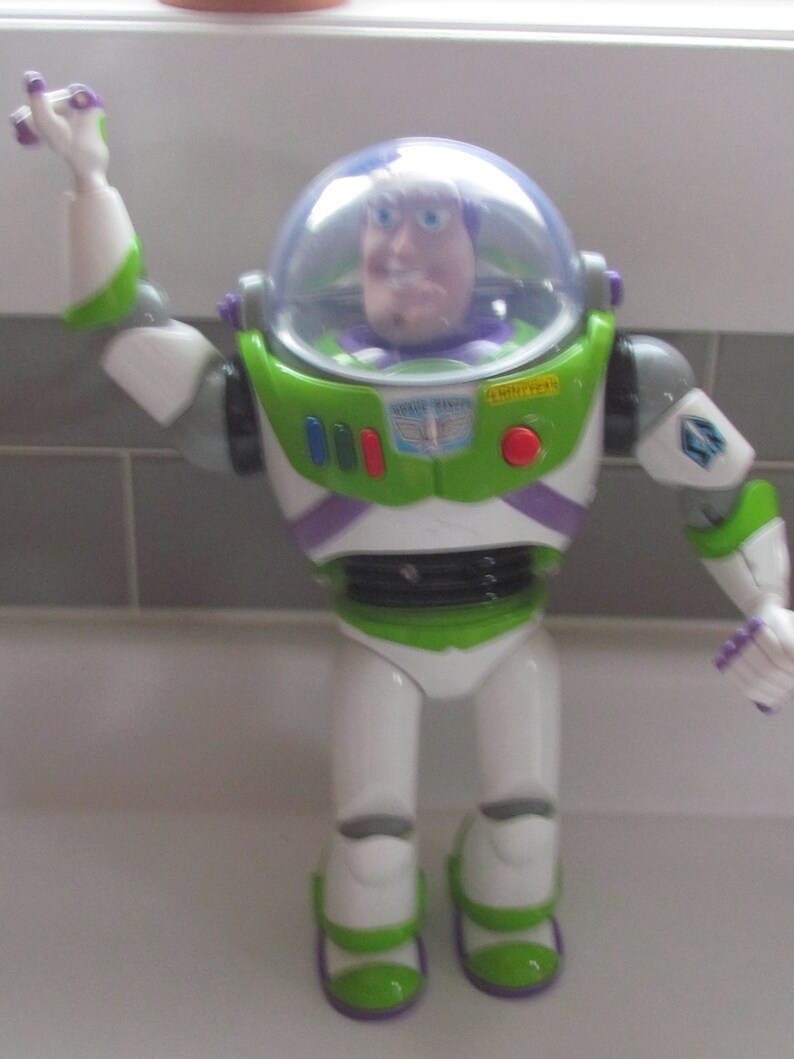 Puede incluir: Figura de acci&oacute;n de Buzz Lightyear de la franquicia Toy Story. La figura es principalmente blanca, verde y morada, con un casco de pl&aacute;stico transparente. Tiene brazos y piernas articulados, y la cara de Buzz Lightyear es visible dentro del casco.