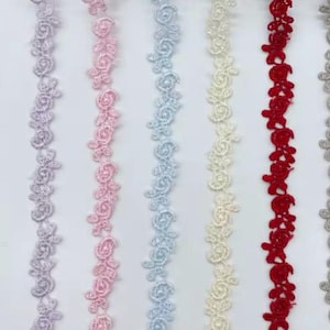 May include: A collection of floral lace trim in various colors. The trims feature a repeating pattern of roses and leaves. Colors include lavender, pink, light blue, cream, red, and gray. The lace is likely used for sewing, crafting, or embellishing garments.