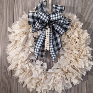 May include: A white fabric wreath with a black and white checkered bow and a strand of wooden beads.