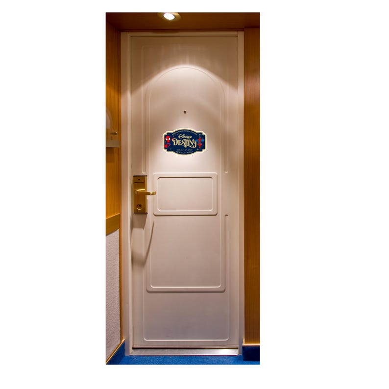 Puede incluir: Una puerta blanca con un pomo dorado rectangular y un letrero decorativo centrado en el panel superior. El letrero es azul oscuro con letras doradas que dicen Disney DESTINY, flanqueado por peque&ntilde;os iconos de Spider-Man en rojo y azul.