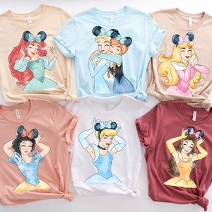 May include: Six different t-shirts featuring Disney princesses with mouse ears. The shirts are in various colors, including beige, light blue, pink, peach, white, and maroon.