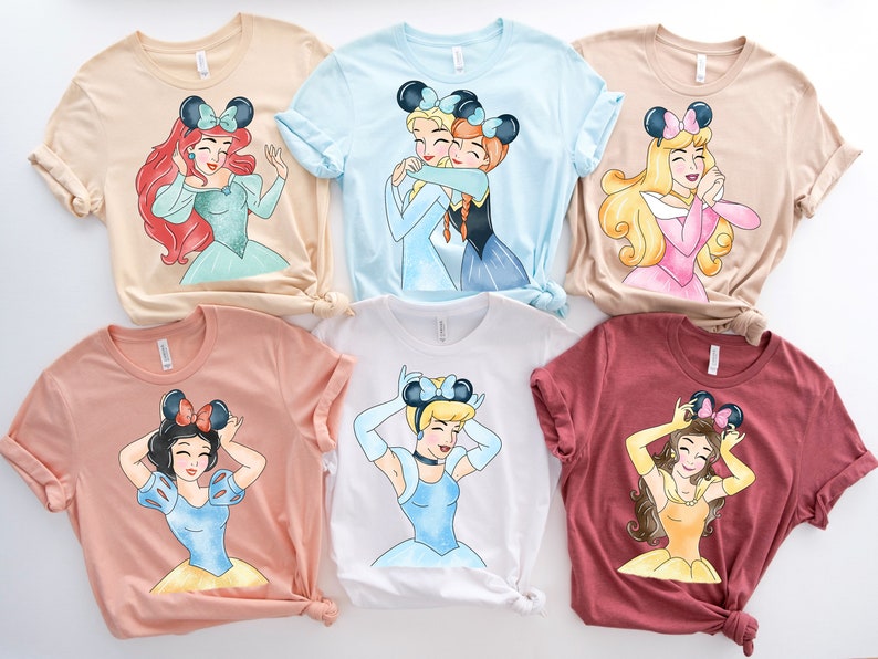May include: Six different t-shirts featuring Disney princesses with mouse ears. The shirts are in various colors, including beige, light blue, pink, peach, white, and maroon.