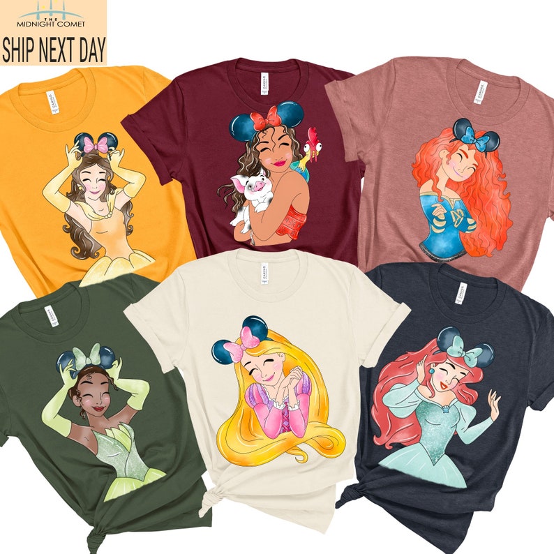 May include: Six different t-shirts featuring Disney princesses with mouse ears. The princesses are Belle, Tiana, Ariel, Rapunzel, Mulan, and Pocahontas. Each shirt is a different color: yellow, maroon, pink, beige, green, and navy.
