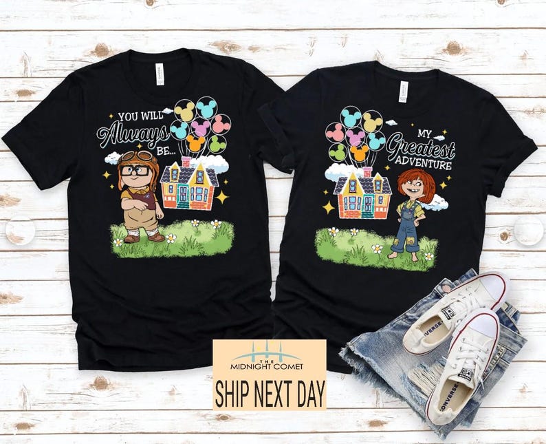 May include: Two black t-shirts with cartoon graphics. One shirt features a character with the text "You Will Always Be..." and a house with balloons. The other shirt says "My Greatest Adventure" with a character and house.